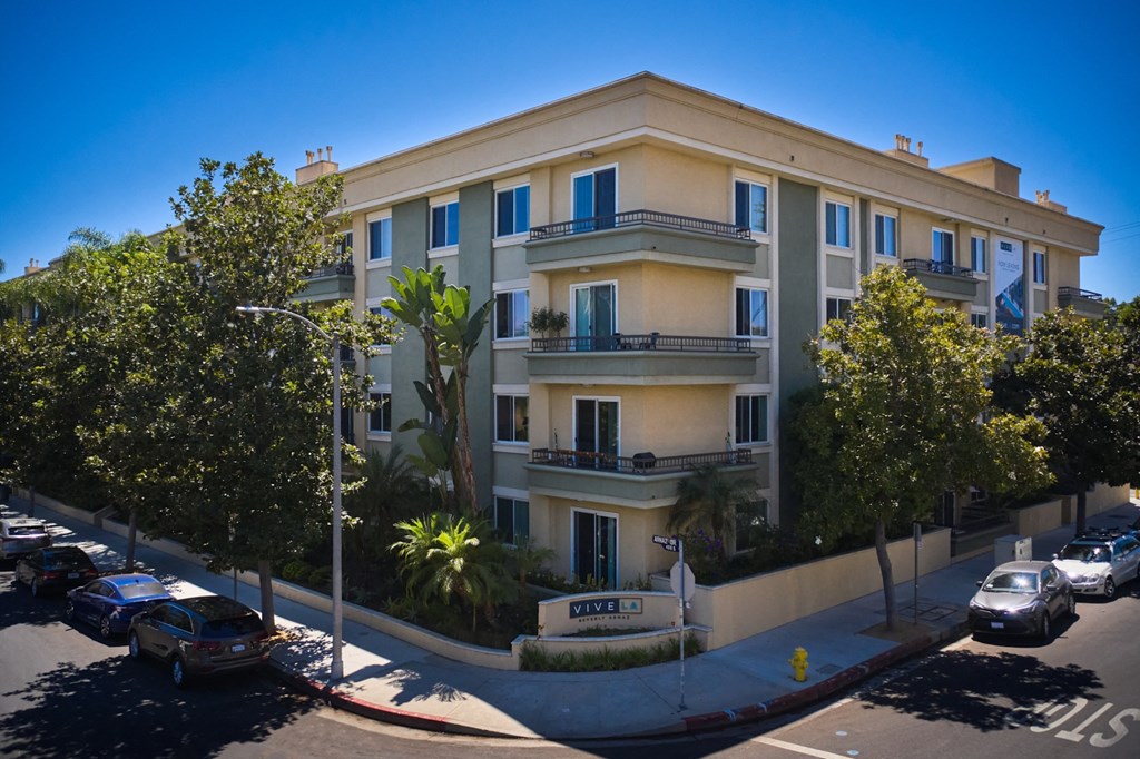 Exterior of building surrounded by trees and sidewalk, balconies wrapping around corners