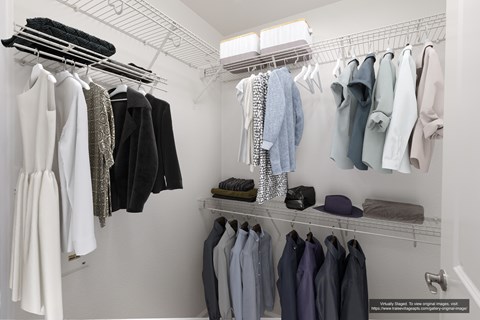 A white closet with clothes hanging on shelves and hangers.