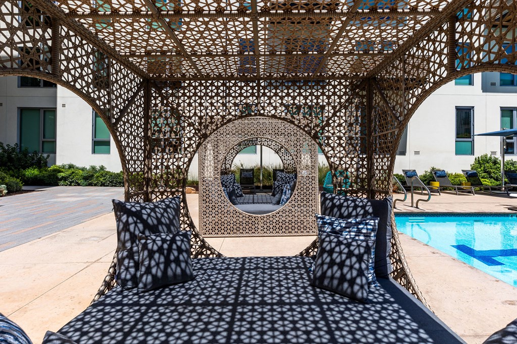 a seating area with pillows and a pergola next to a pool