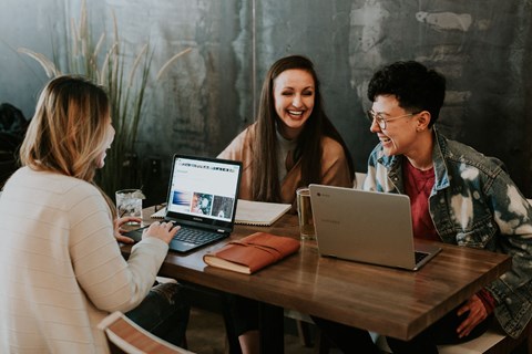 three people sitting at a table with laptops