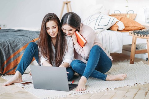 two young women sitting on the floor looking at a laptop computer