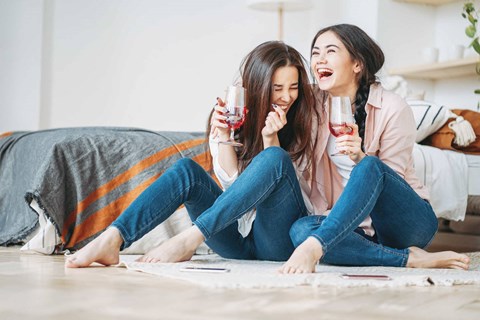 two women sitting on the floor with wine glasses
