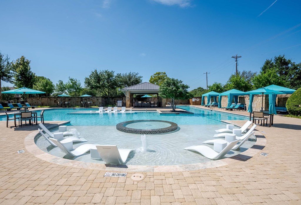 a resort style pool with white chairs and blue umbrellas at Discovery at Craig Ranch, McKinney