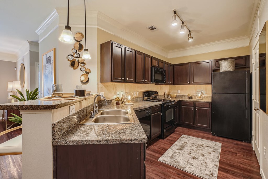 a kitchen with espresso color cabinets, granite countertops, designer lighting fixtures and black appliances  at Grand Villas Apartments, Katy
