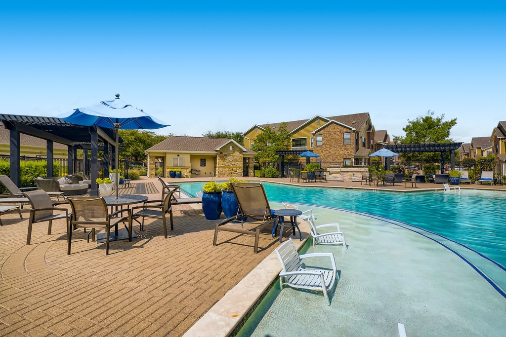 a swimming pool with chairs and umbrellas next to club house at Grand Villas Apartments, Katy, Texas