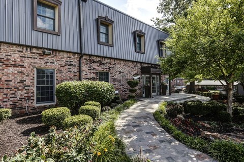 A building with a grey roof and a brick wall with a garden in front.