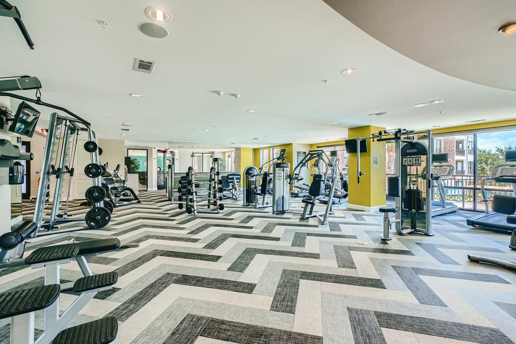 a gym with weights and cardio machines and a large window at Imperial Lofts, Sugar Land