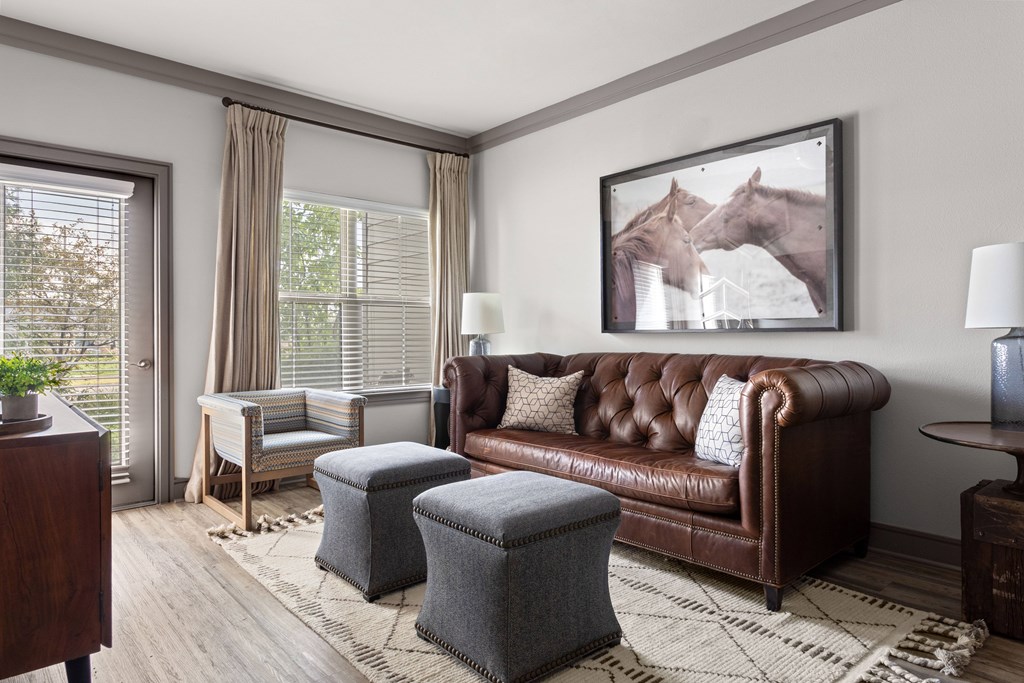 A brown leather couch sits in a living room with a framed picture of two horses on the wall above it.