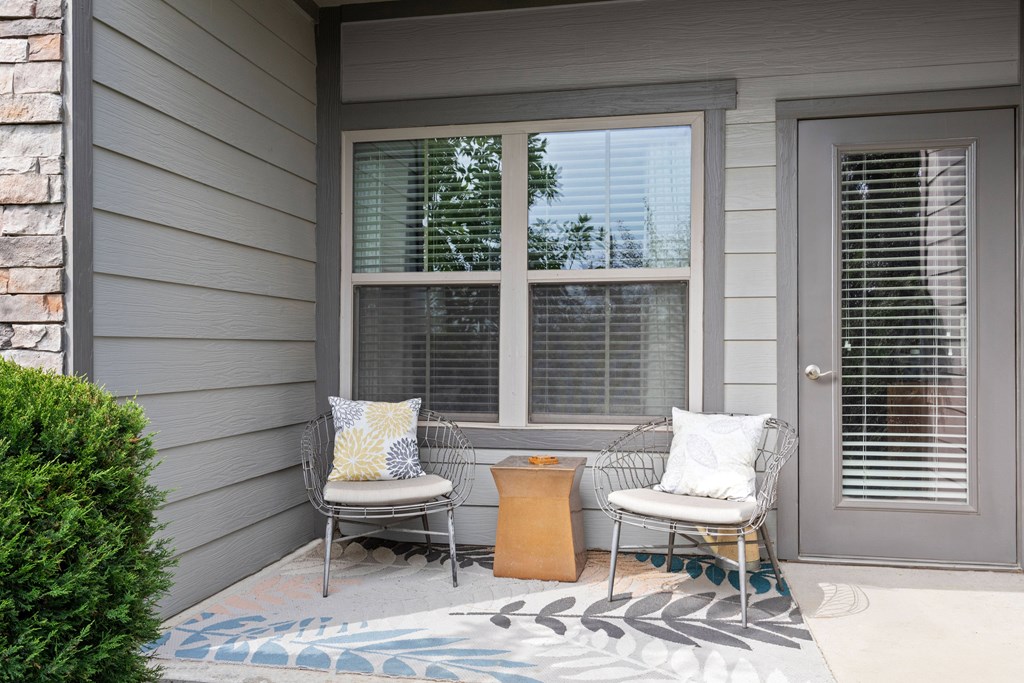 A house porch with two chairs and a pillow on them.