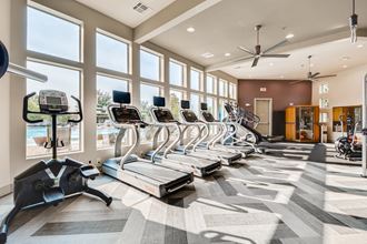 a gym with plenty of cardio equipment and windows