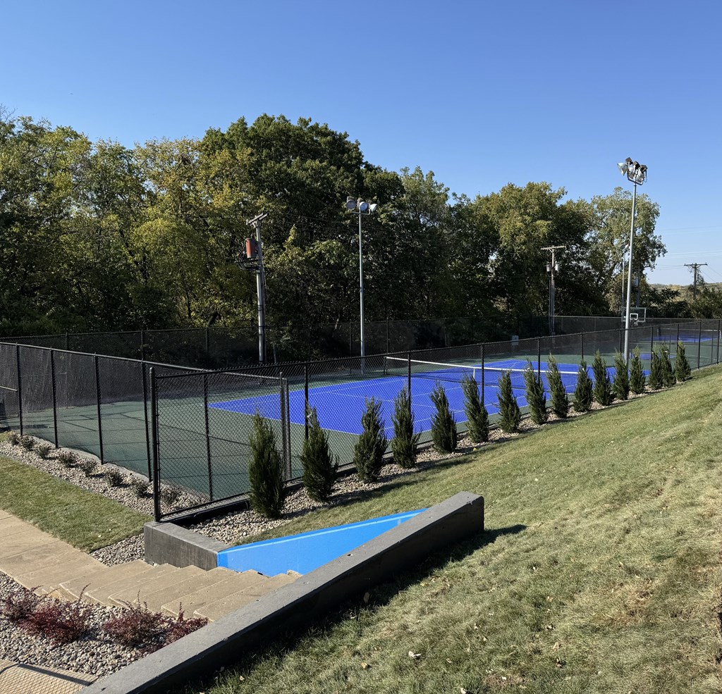 a tennis court with a fence around it and a blue pool at The Boulevard, Roeland Park, KS
