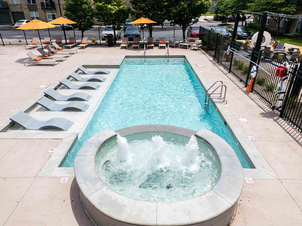 A fountain in the middle of a pool surrounded by lounge chairs.