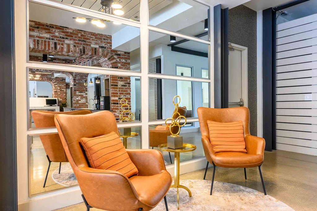 Three orange chairs are arranged around a small table in a room with a brick wall.
