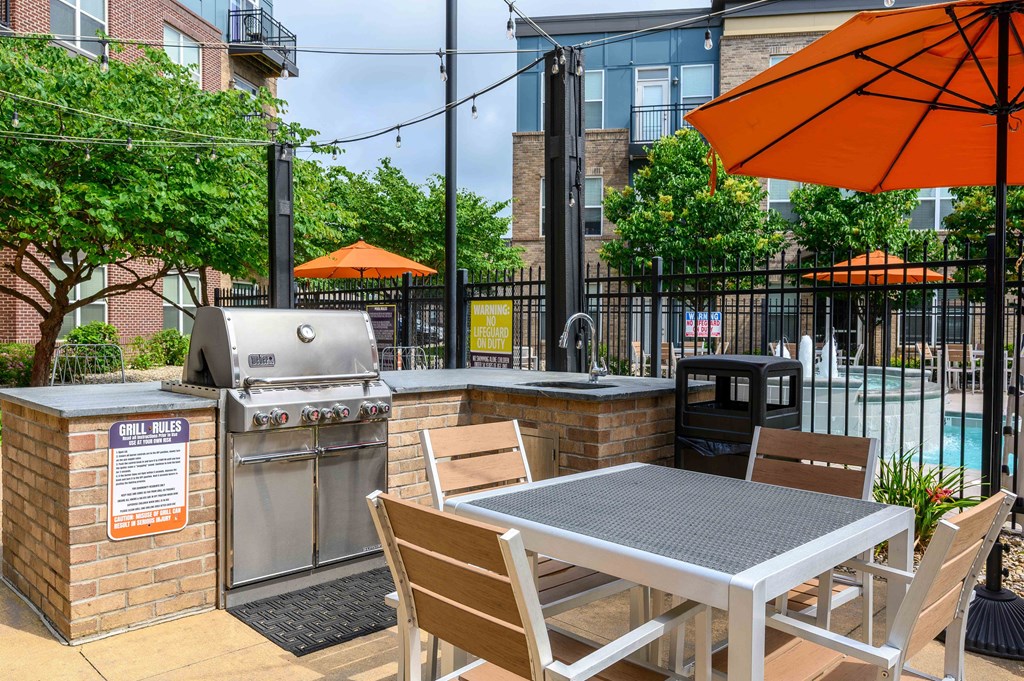 A BBQ grill is on a patio with a table and chairs.