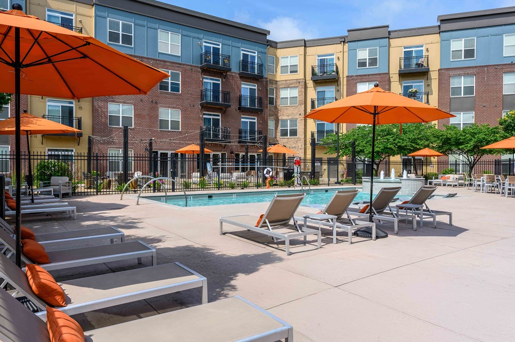 A pool area with sun loungers and umbrellas in front of apartment buildings.