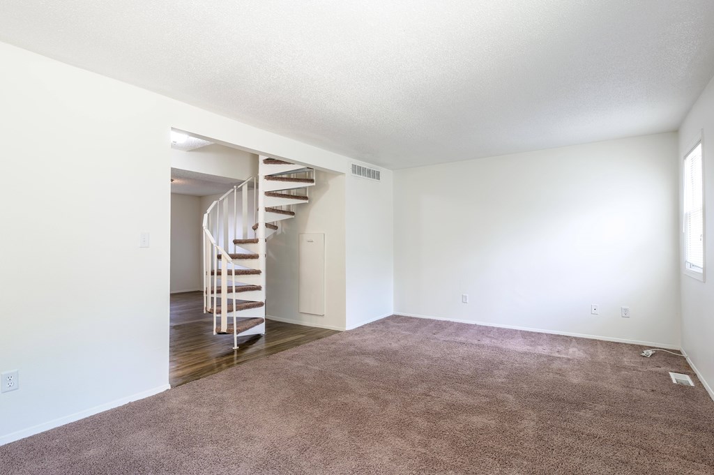 A room with a carpeted floor and a spiral staircase at Spring Creek Townhomes Apartments, Springfield, IL 62702