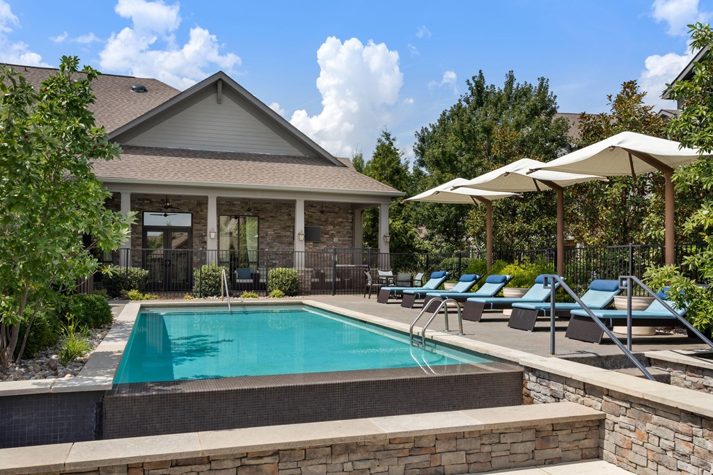 A pool with a house and sun loungers in front.