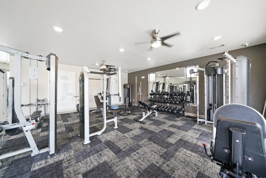a gym with weights and cardio machines and a ceiling fan  at Grand Villas Apartments, Texas, 77494