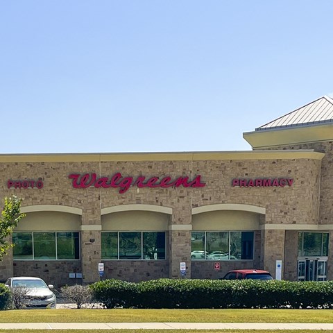 A Walgreens Pharmacy store with a red car parked in front.
