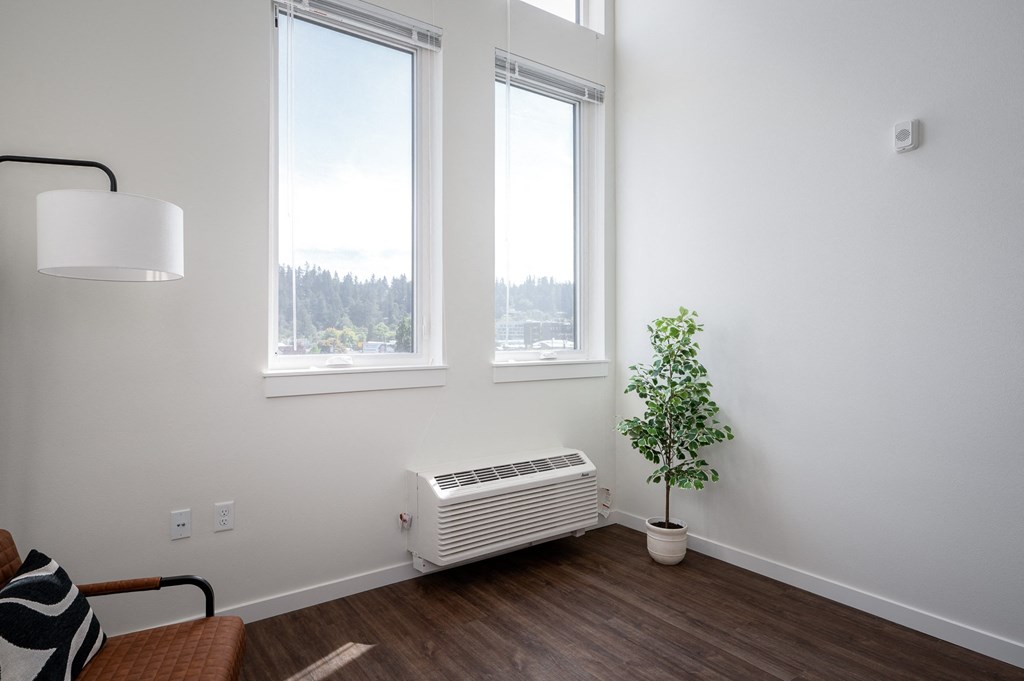 a living room with three windows, an air conditioner,  and a plant