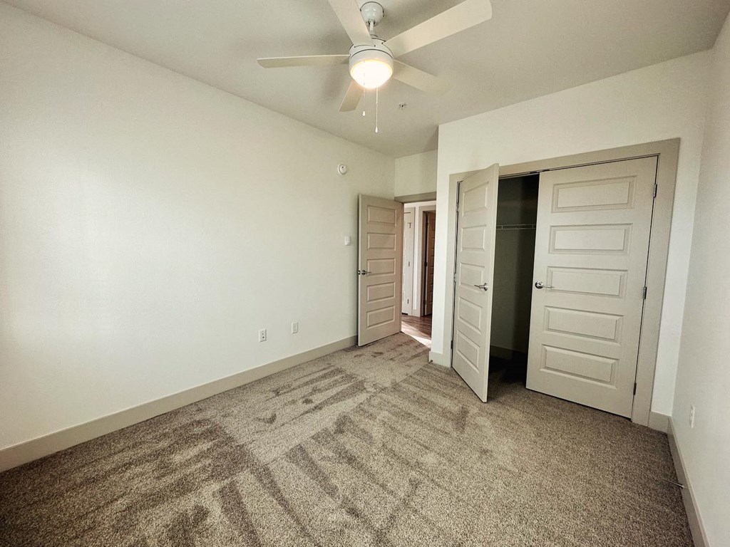 an empty living room with a ceiling fan and a closet