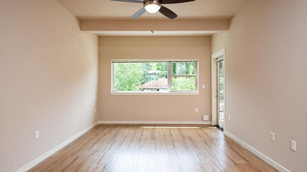 a empty living room with a window and a ceiling fan