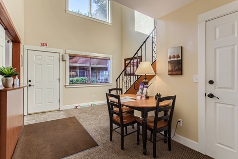 A dining room with a brown rug and a wooden table with chairs.