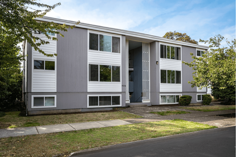 A grey and white building with a tree in front.