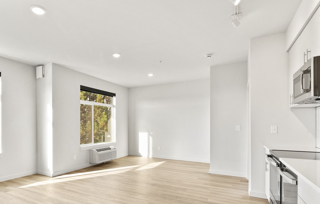 an empty living room with a window and a kitchen