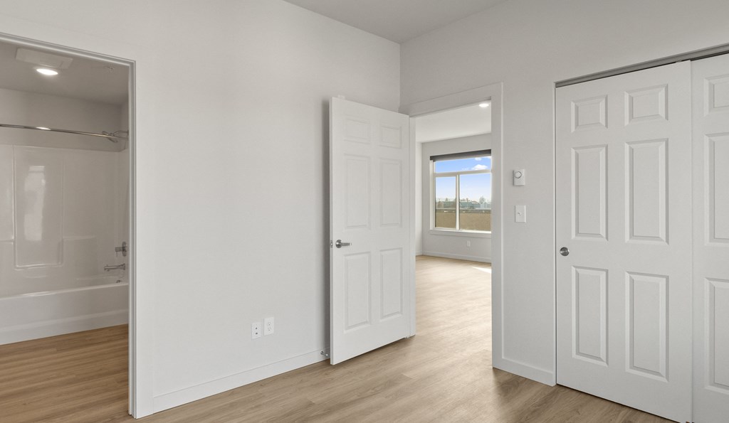 an empty bedroom and bathroom with white doors and wood flooring