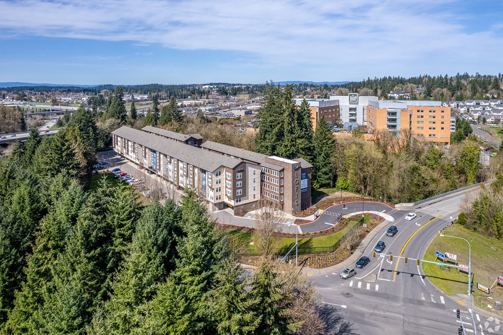 Apartments for Rent in Vancouver, WA -134th Street Lofts - Aerial View of Apartment Complex with Brown and Tan Walls, Surrounded by Lush Greenery.