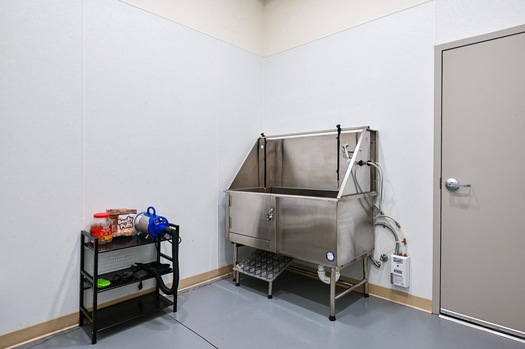 a stainless steel tub in a white room with a black cart next to it