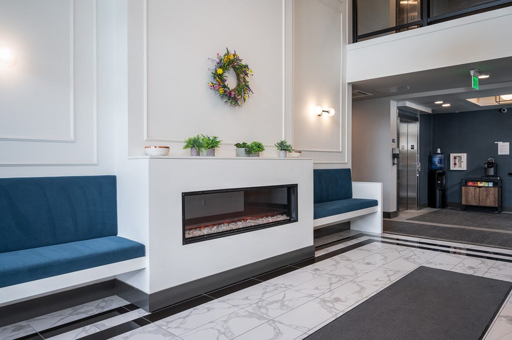 a fireplace in the lobby of a building with blue chairs and a wreath on the wall