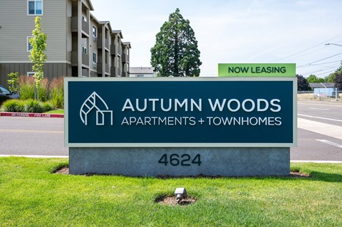 A sign for Autumn Woods Apartments and Townhomes is displayed in front of a building.