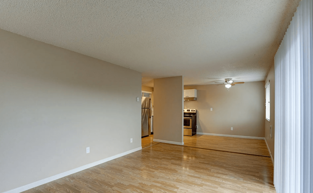 an empty living room with a hard wood floor and a kitchen