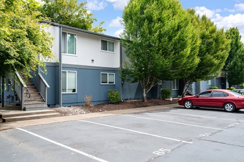 A red car is parked in a parking lot in front of a two-story building.