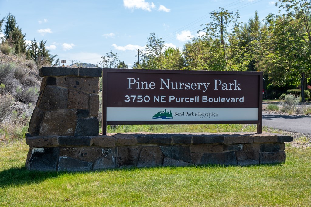 A sign for Pine Nursery Park stands in front of a grassy area.