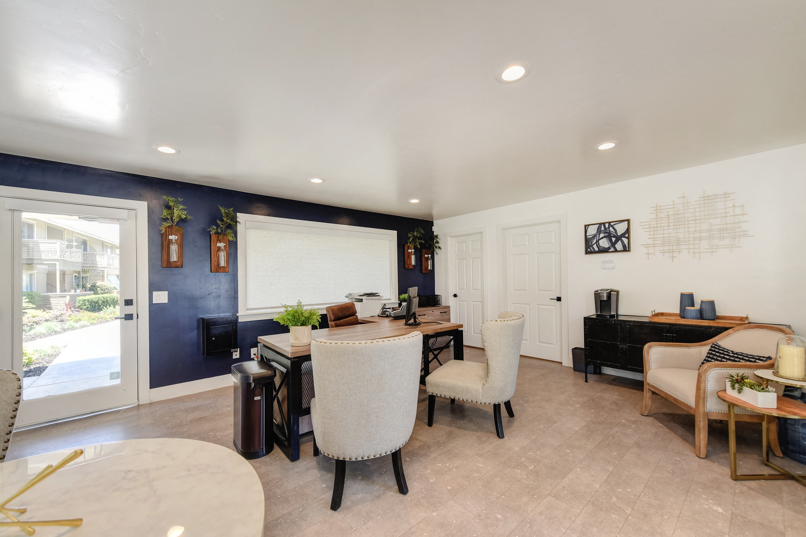 Inside Manager and  Leasing Office. Desk with two chairs in front of it. Additional seating with small round table in the foreground and to the right.