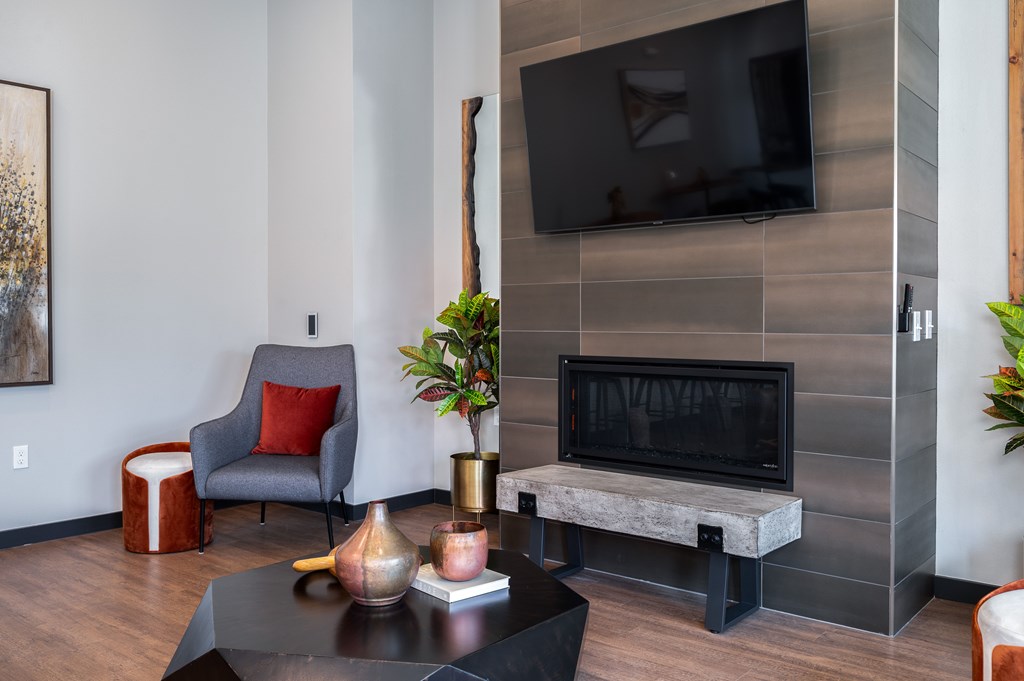 A grey chair with a red pillow sits in front of a grey wall with a flat screen TV mounted on it.