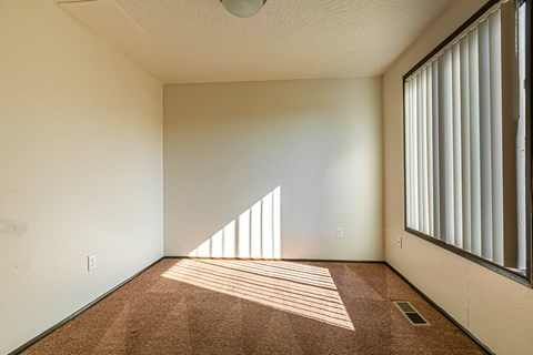 A room with a carpeted floor and a window with blinds.