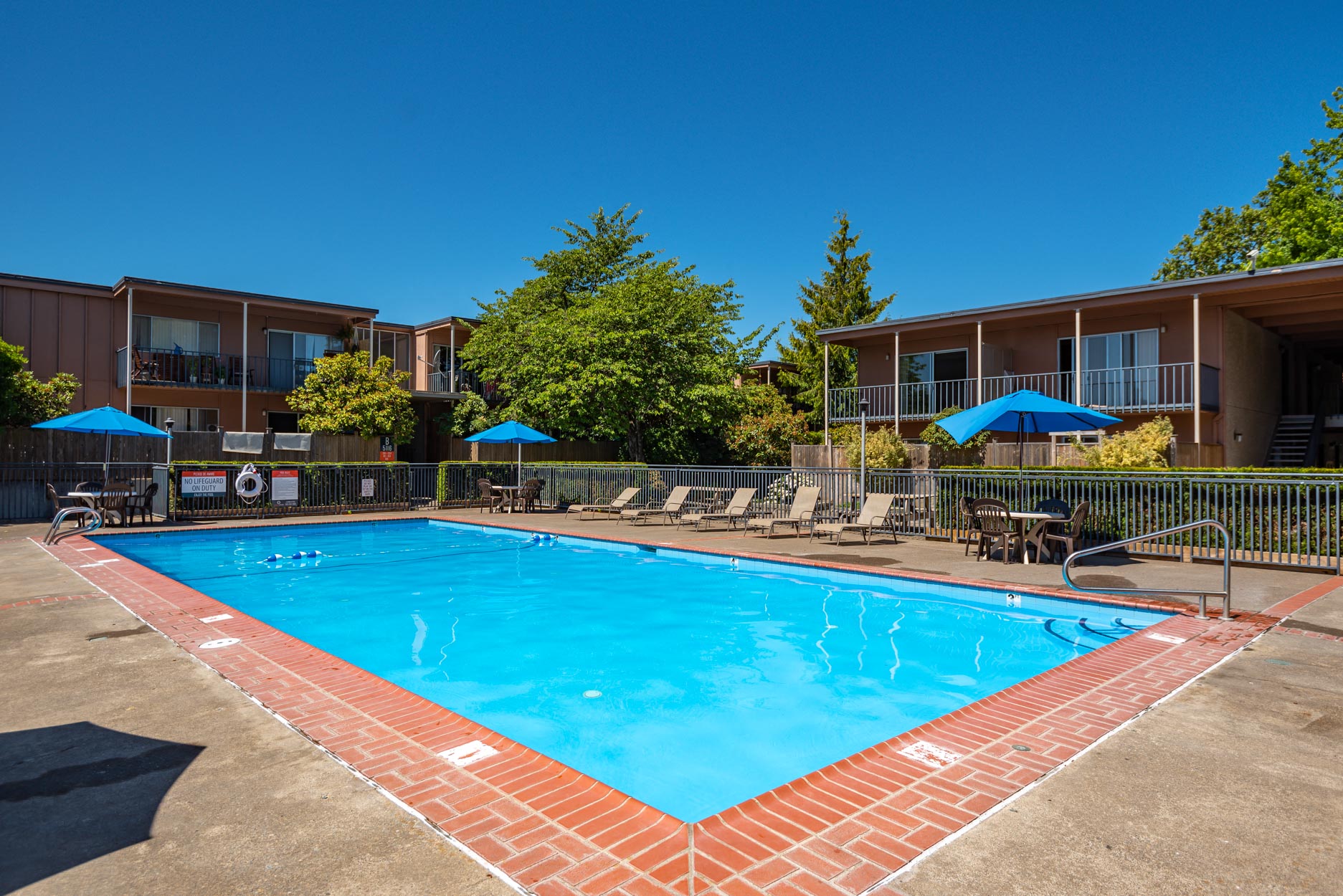outdoor pool with seating around and blue umbrellas over tables.