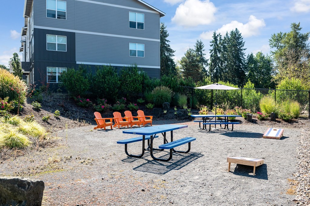 A picnic area with tables and chairs in front of a grey building.