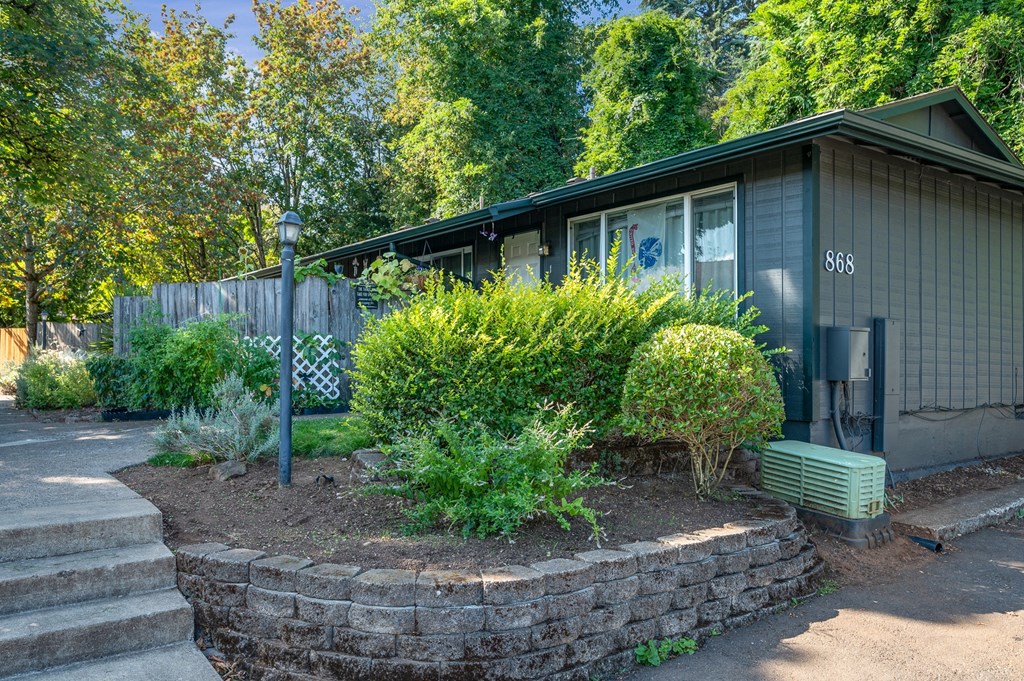 a house with a stone retaining wall and bushes in front of it