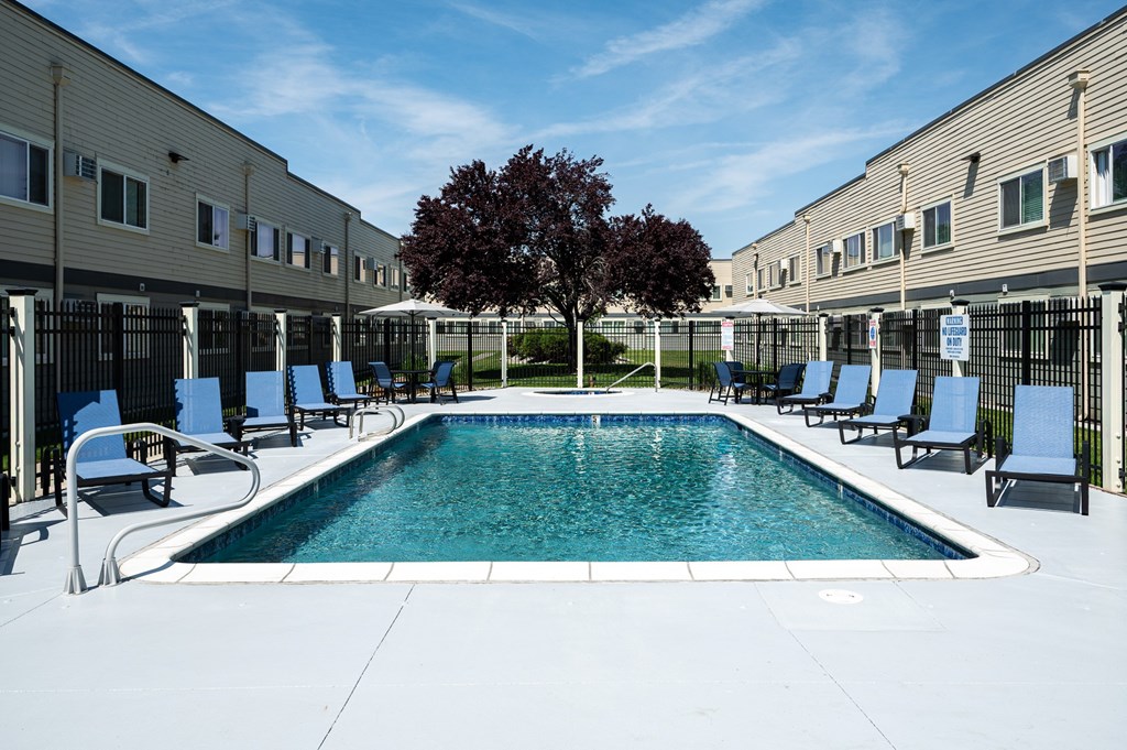 A swimming pool surrounded by chairs and a tree in a sunny courtyard.