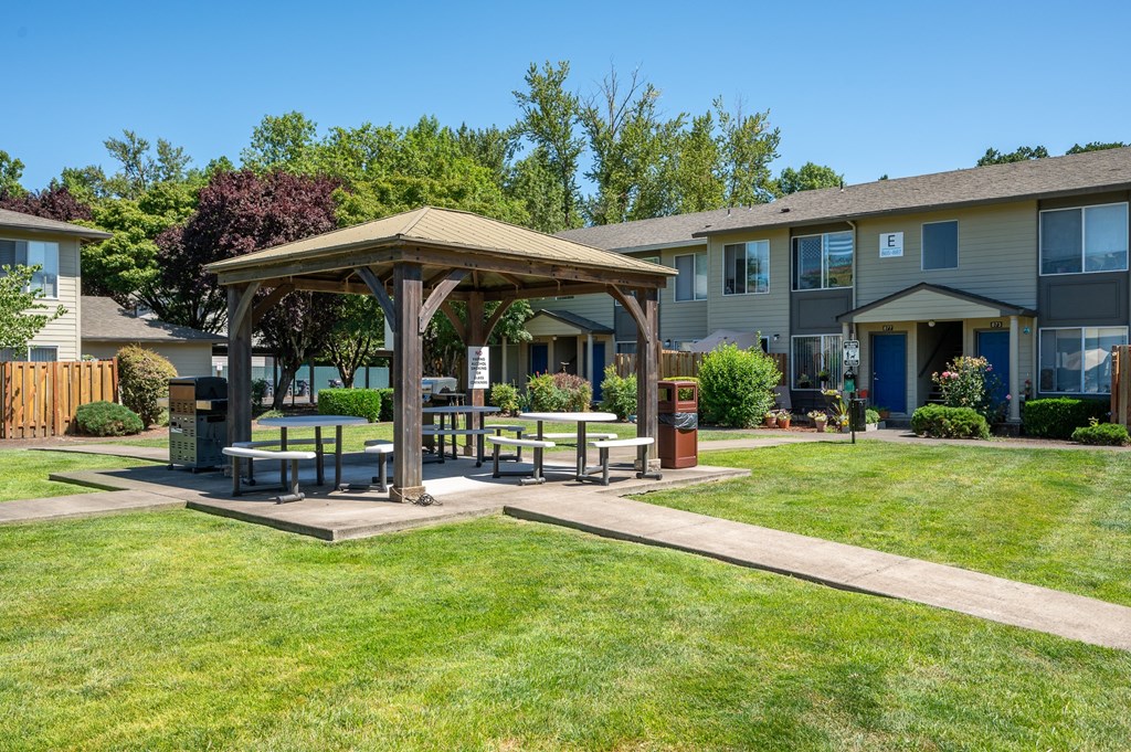 A gazebo is surrounded by a grassy area in front of apartment buildings.