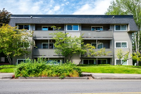 the front of a gray apartment building with green grass and trees