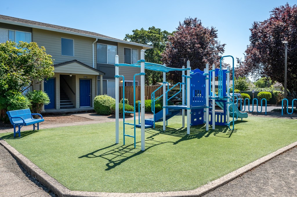 A playground with a blue slide and a blue bench in front of a building.