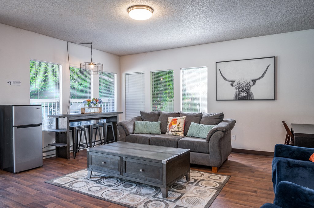 a living room with a couch and a coffee table and a kitchen with a refrigerator