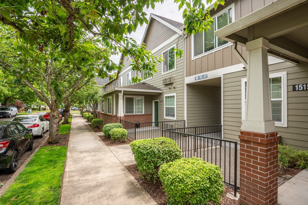 a sidewalk in front of a row of houses with cars parked in front