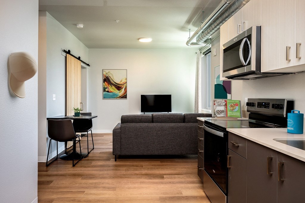 A modern kitchen with a grey couch and a black TV.